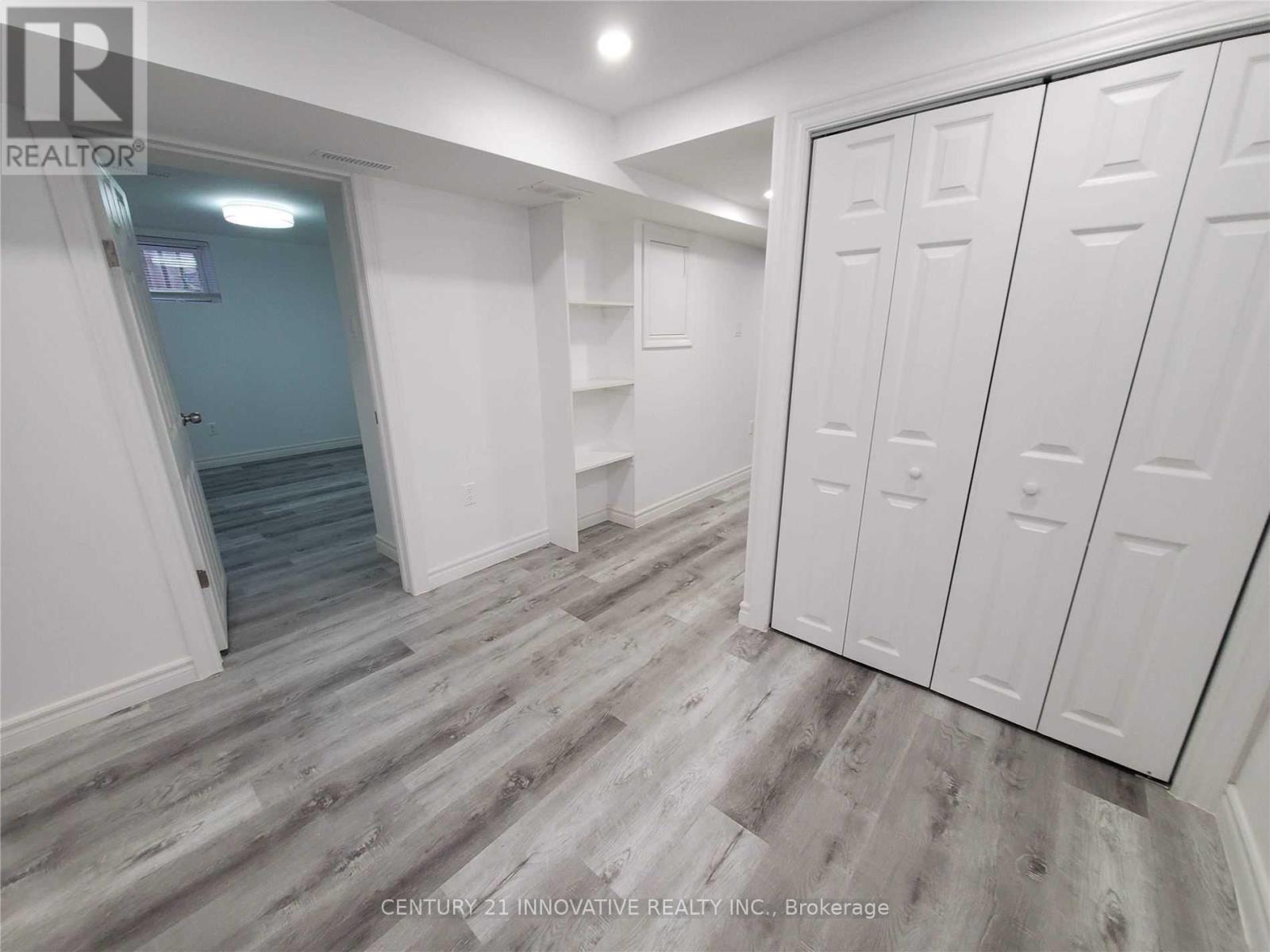 A room with white walls and a wooden floor with a set of white cupboards.