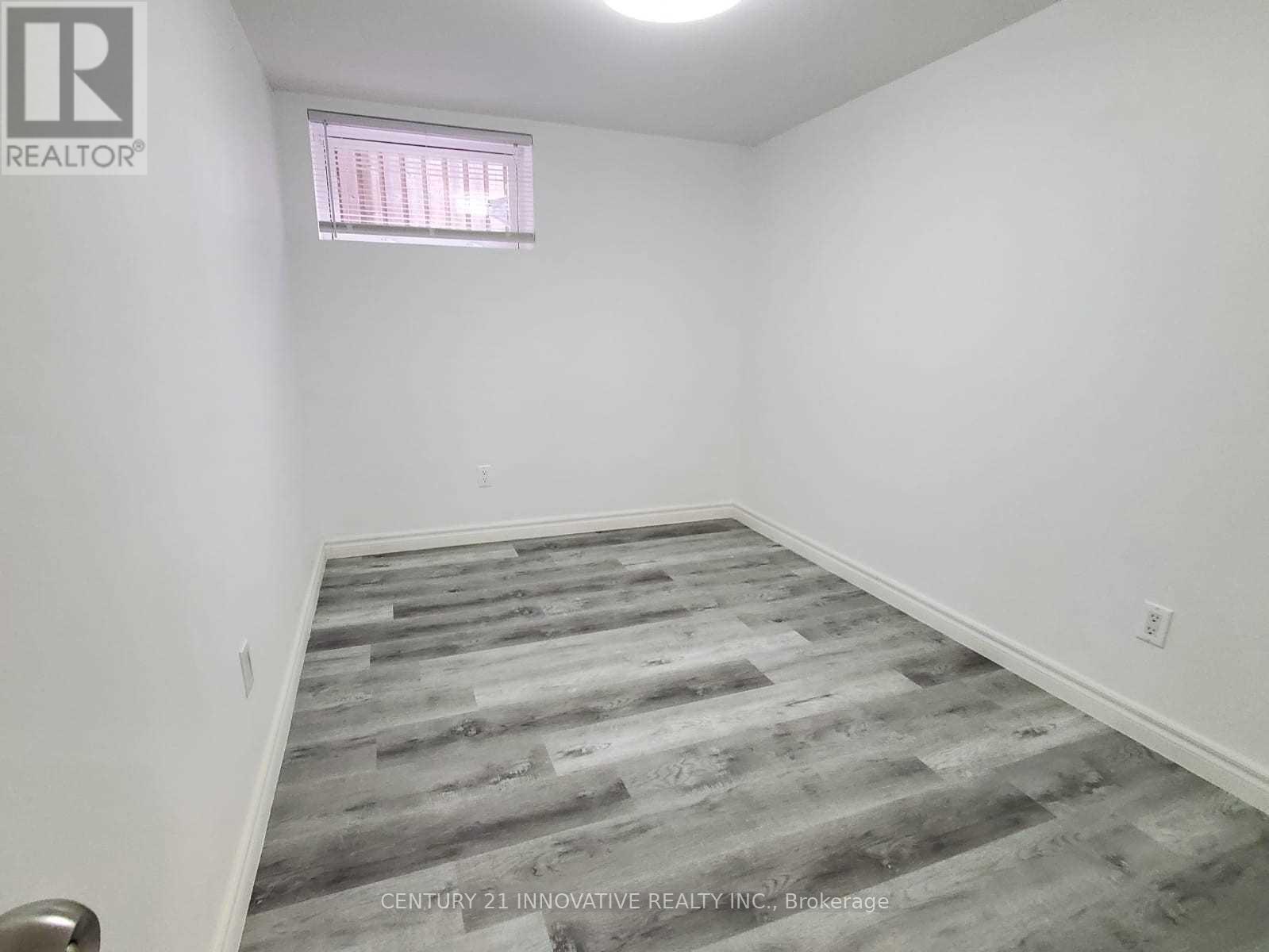 A room with a grey wooden floor and a window with blinds.