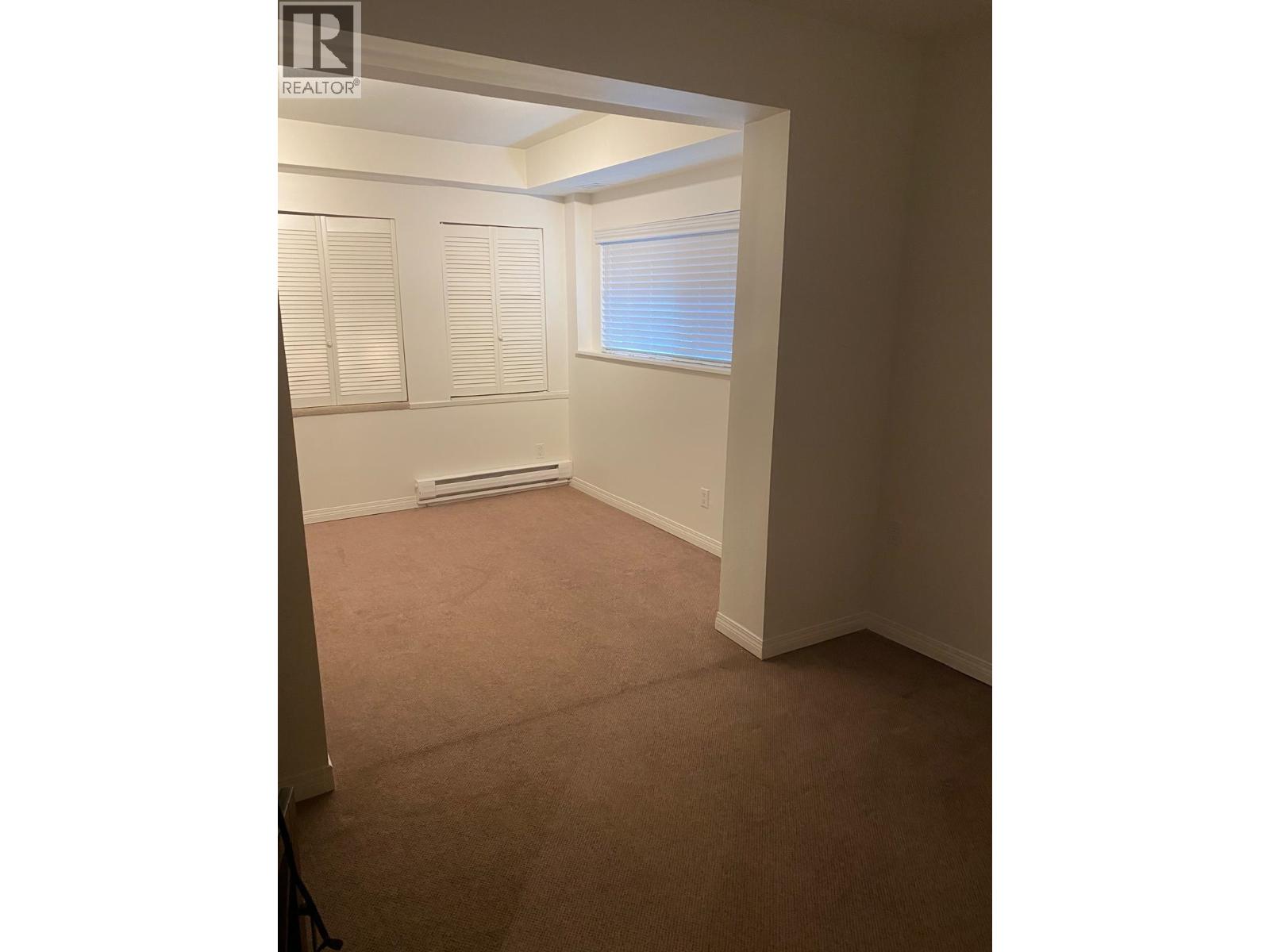 A room with a carpeted floor and a window with blinds.