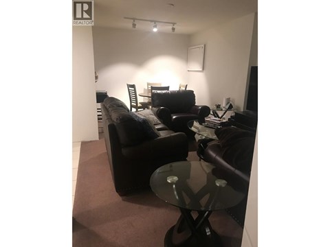 A living room with a black couch and a glass table.