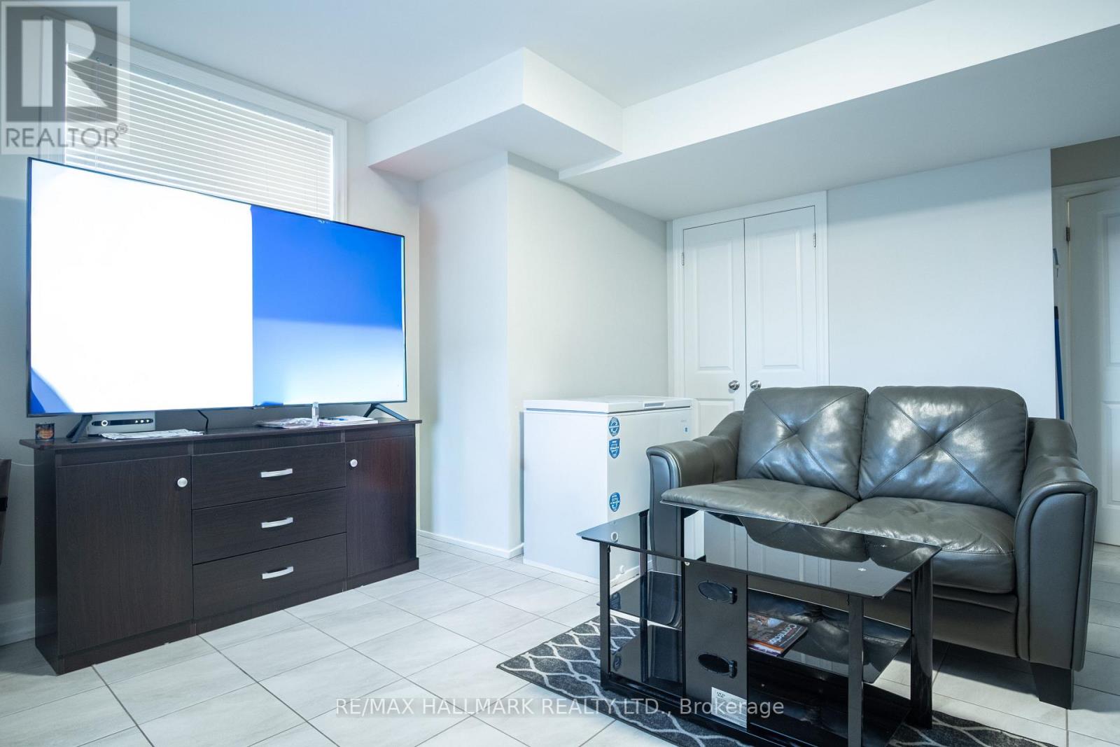 A living room with a black leather couch, a flat screen TV, and a coffee table.