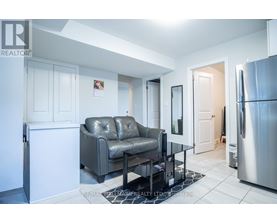 A modern kitchen with a grey leather sofa and a stainless steel refrigerator.