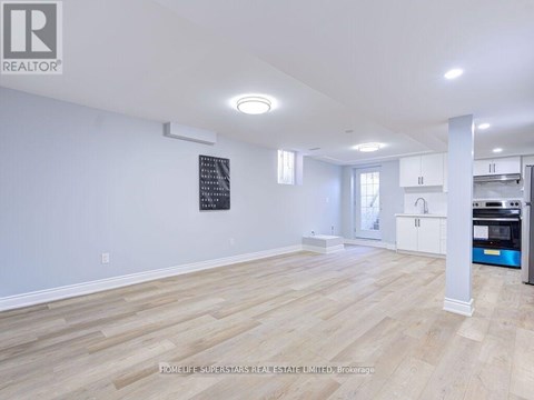 A spacious room with wooden flooring and white walls, featuring a kitchen area with white cabinets and a microwave.
