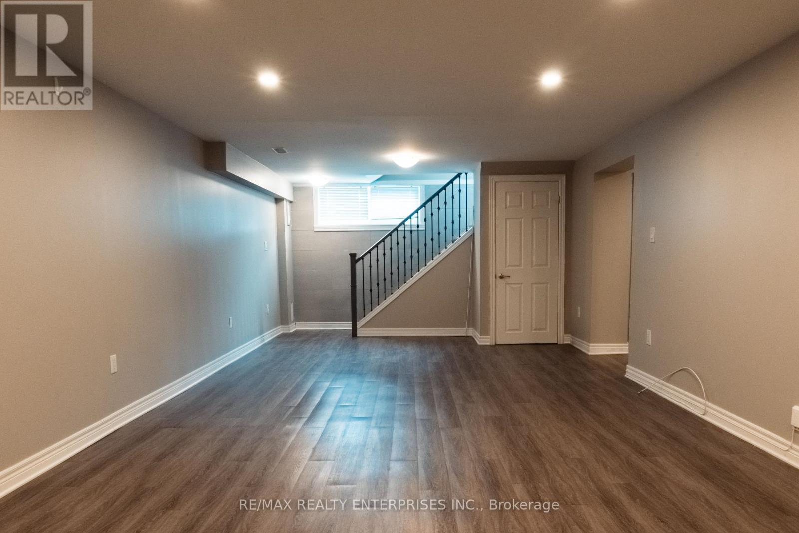 A spacious room with wooden flooring and a staircase leading to another room.