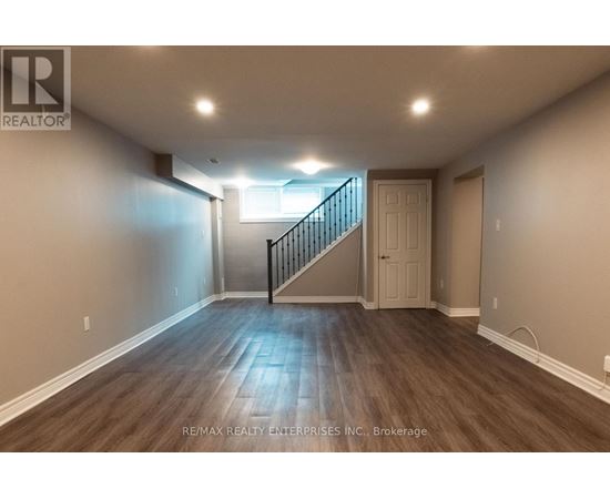 A spacious room with wooden flooring and a staircase leading to another room.
