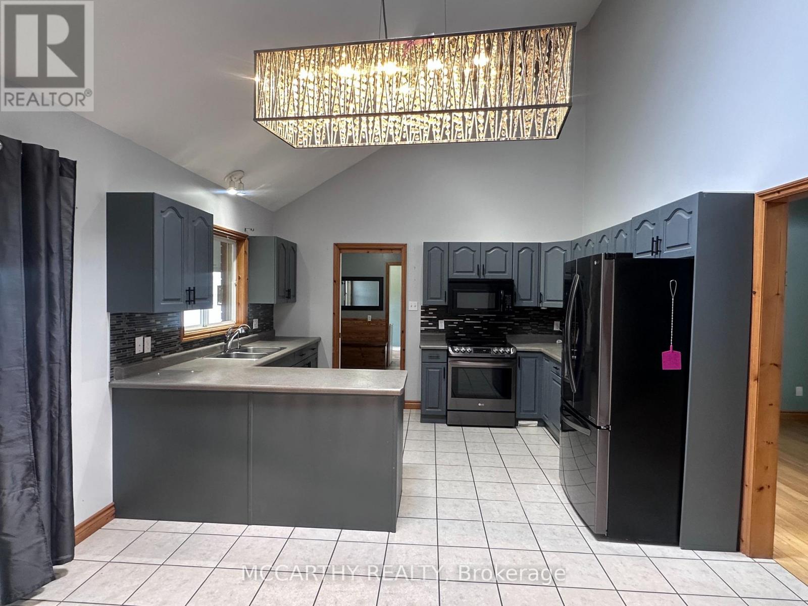 A kitchen with a black refrigerator and a chandelier hanging from the ceiling.