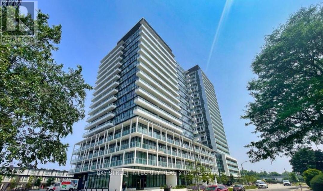 A modern multi-story building with a glass facade is surrounded by trees and has a clear blue sky above.