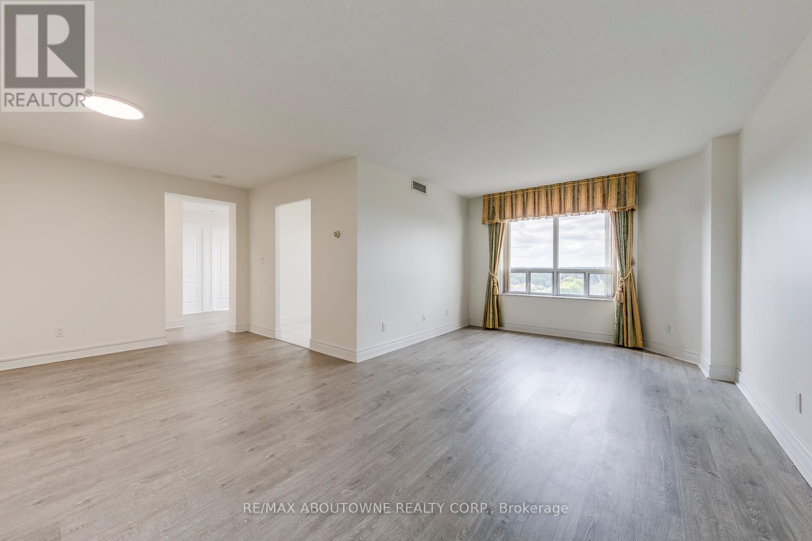 A spacious room with wooden flooring and a window with curtains.