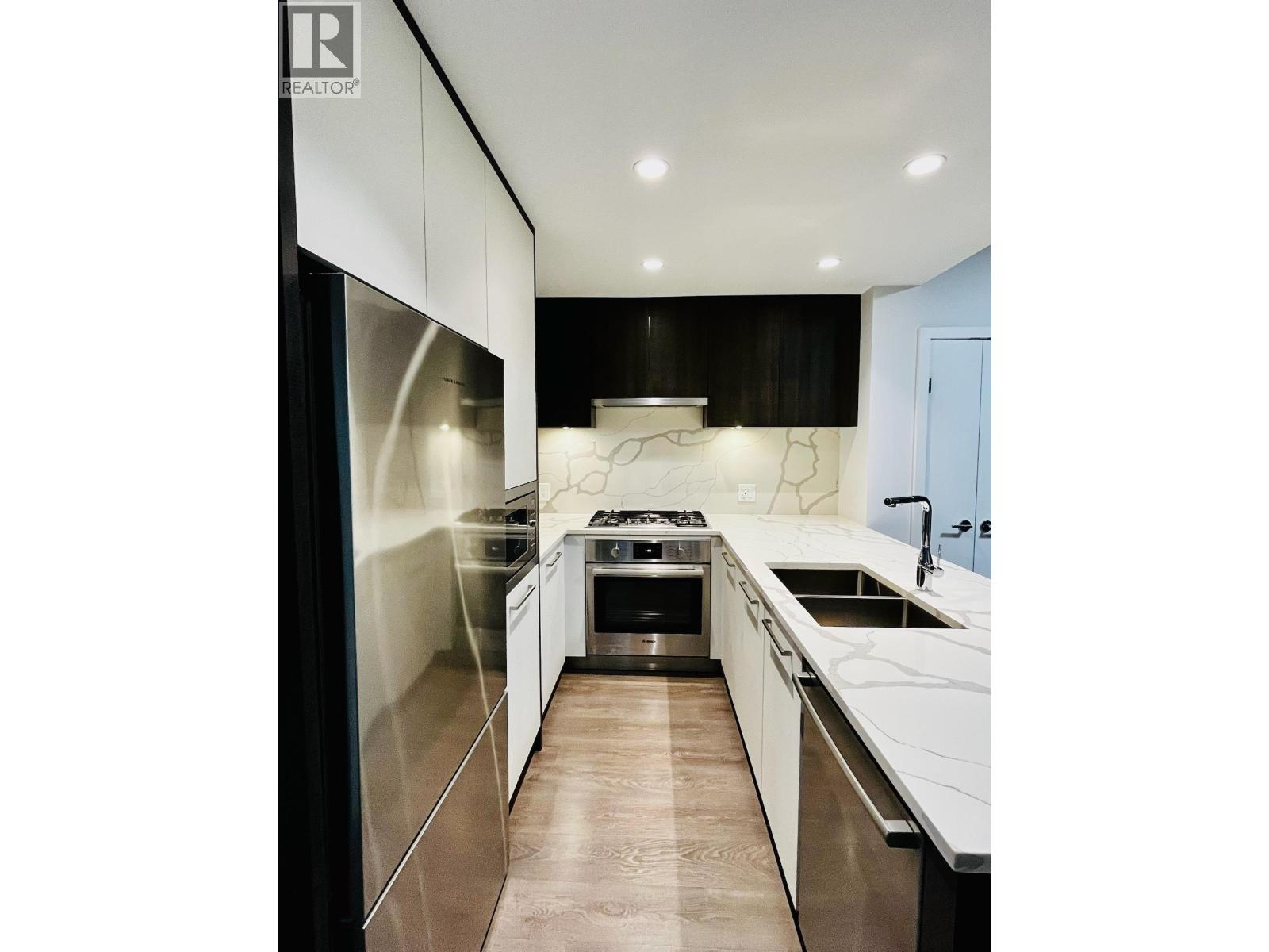 A modern kitchen with a refrigerator on the left and a stove top oven in the middle.