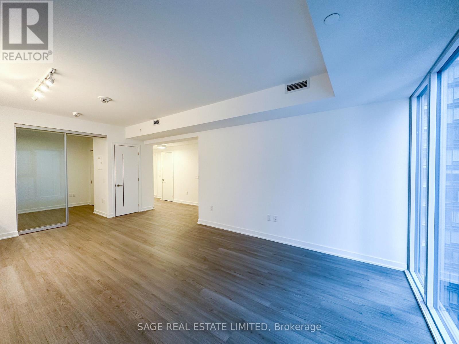 A spacious room with wood flooring and a large window on the right side.