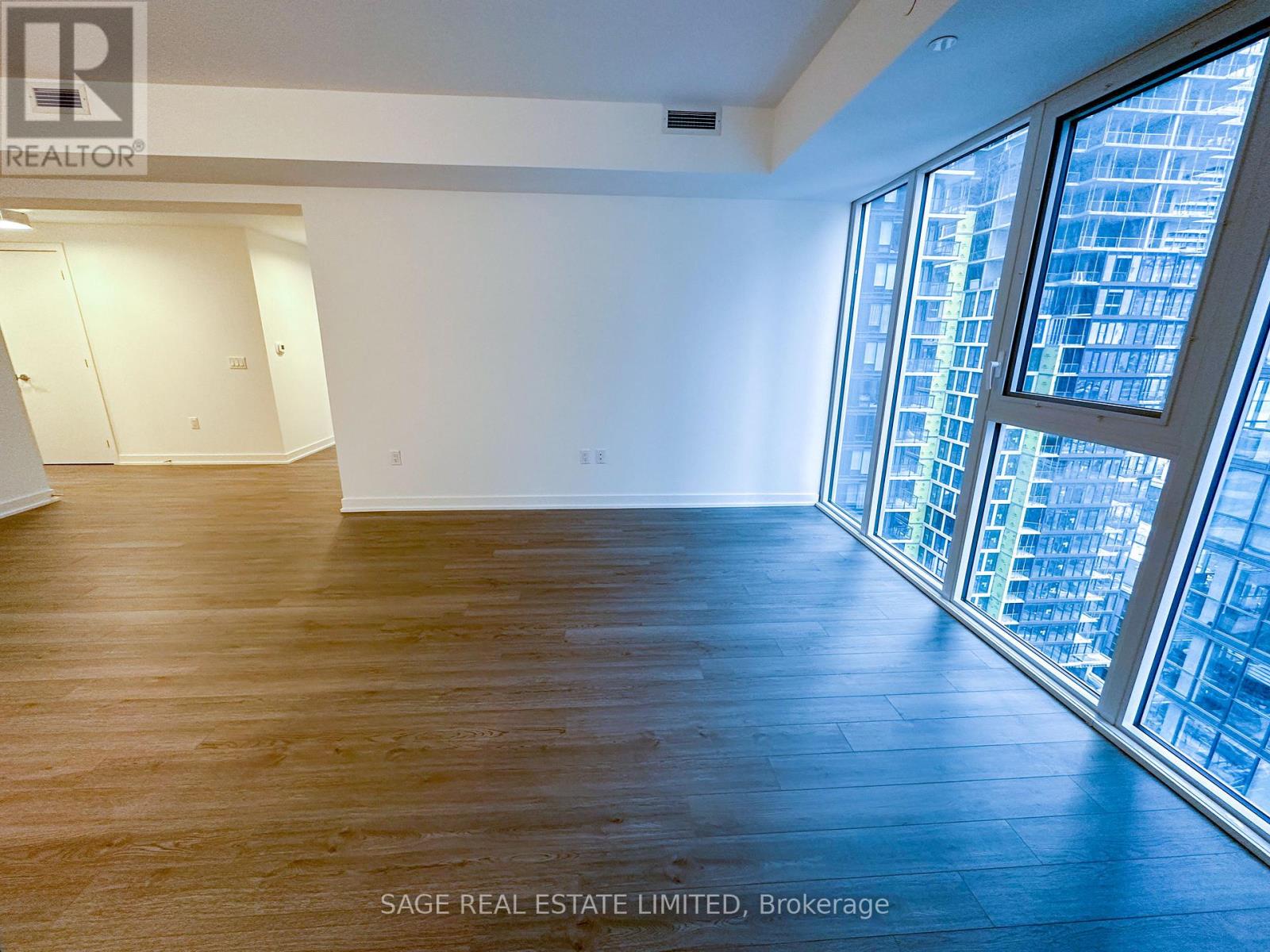 A spacious room with wooden floors and large windows overlooking a cityscape.
