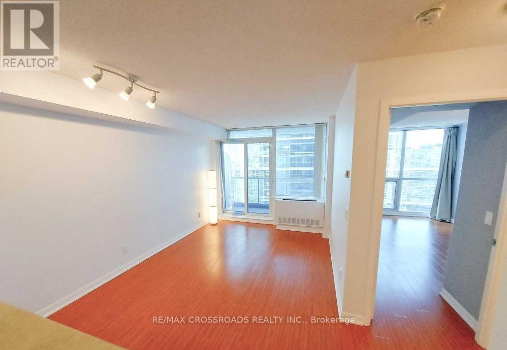 A room with a wooden floor and white walls, with a window that has a view of a building outside.