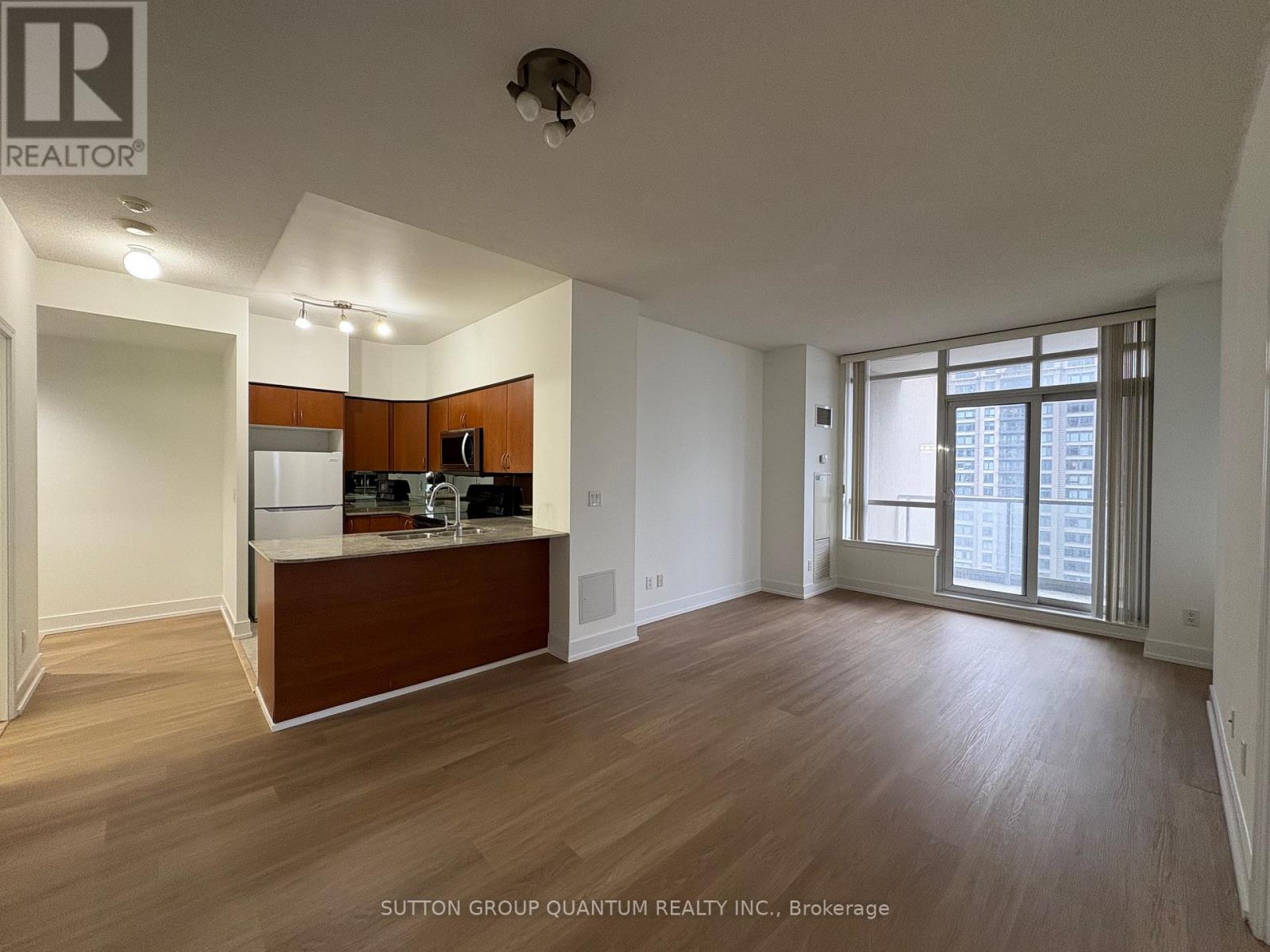 A room with wooden floors and a kitchen area with white appliances.