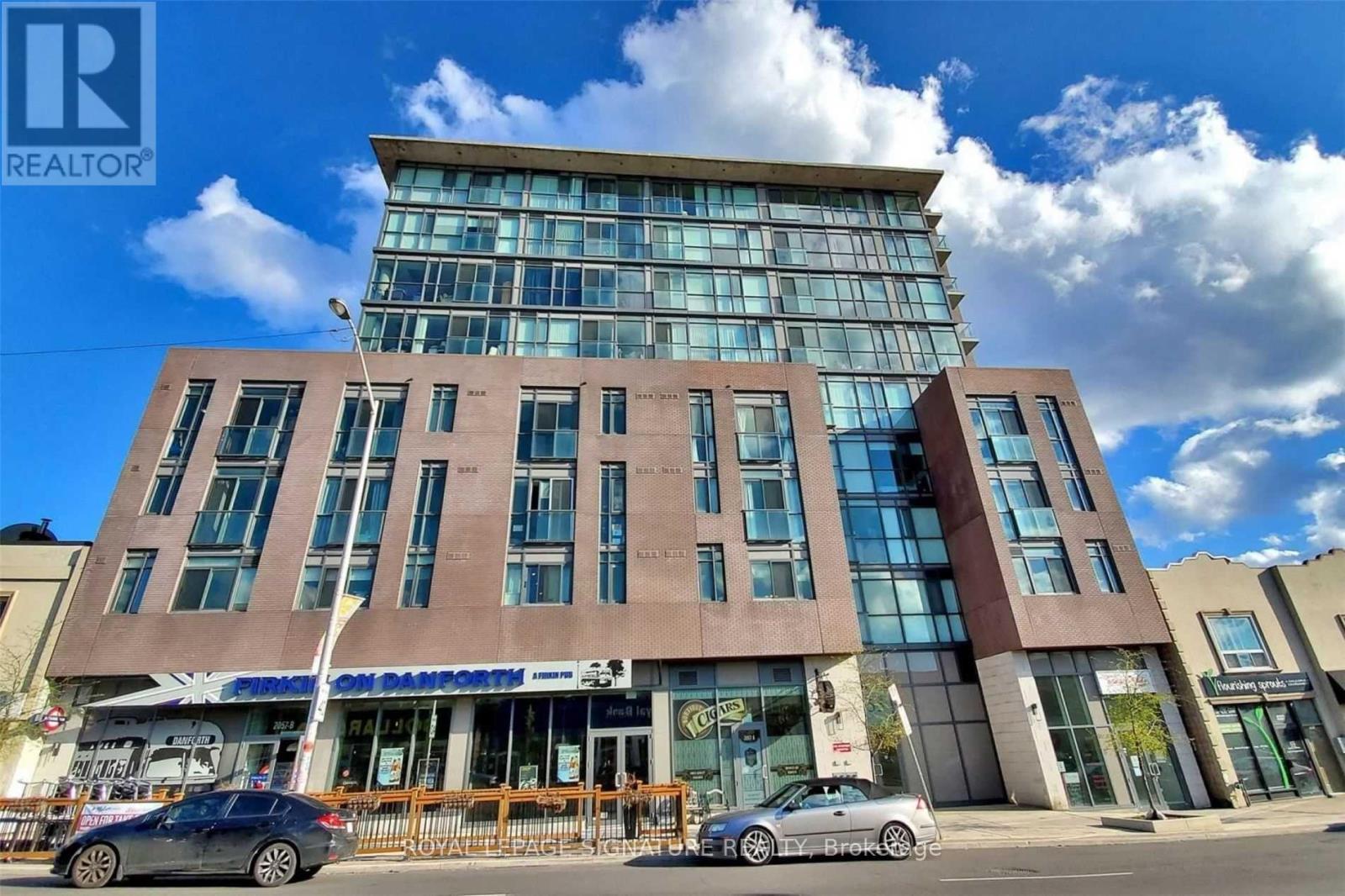 A modern building with a glass facade and a brown exterior is under a blue sky with clouds.