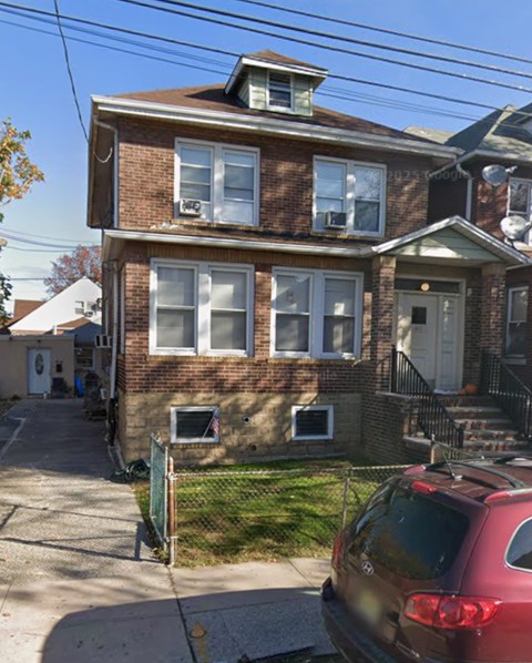 A red car is parked in front of a brick house.
