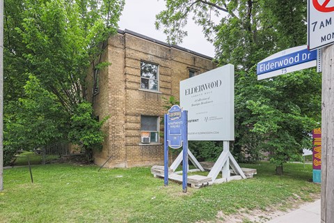 A sign for Elderwood Dr stands in front of a brick building.