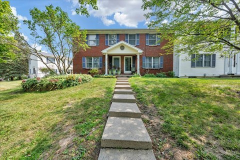 A red brick house with a white fence and a concrete walkway leading to the front door.