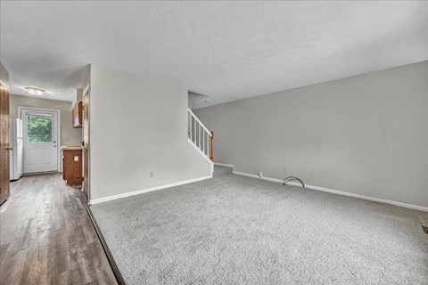 A spacious room with a carpeted floor and a staircase.