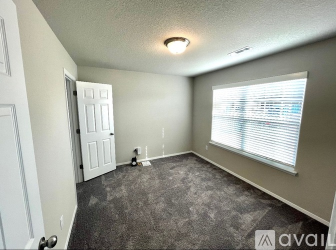 A room with a carpet floor, a door, and a window with blinds.