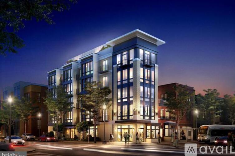 A modern multi-story building with a lit up entrance and a street in front of it.
