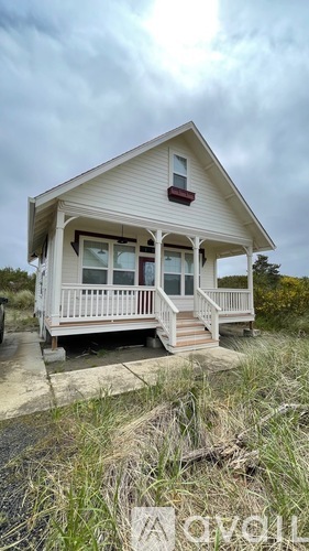 A small white house with a porch and a red awning sits on a grassy area.
