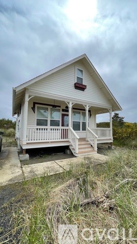 A small white house with a porch and a red awning sits on a grassy area.