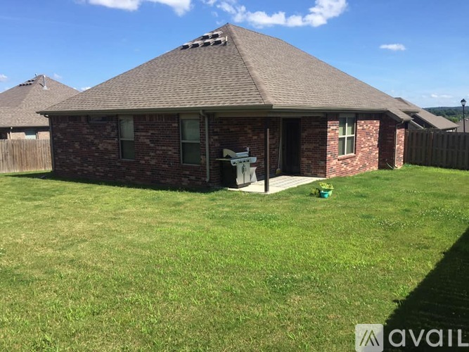 A house with a brown roof and a brick wall is surrounded by a grassy lawn.