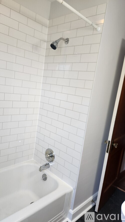 A white tiled bathroom with a white bathtub and a shower head.