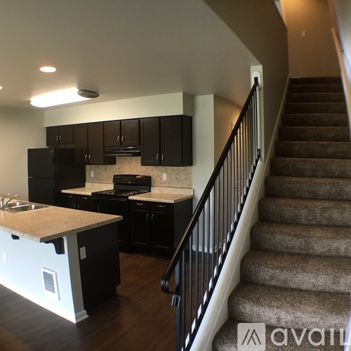 A kitchen with black cabinets and a staircase with a carpeted runner.