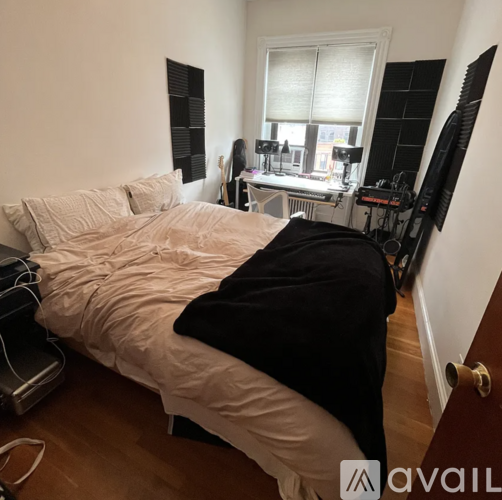 A bedroom with a bed, a desk with a computer, and a window with blinds.