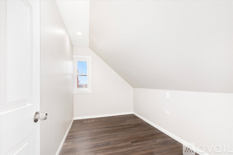 A room with a white door and a window with a view of trees.