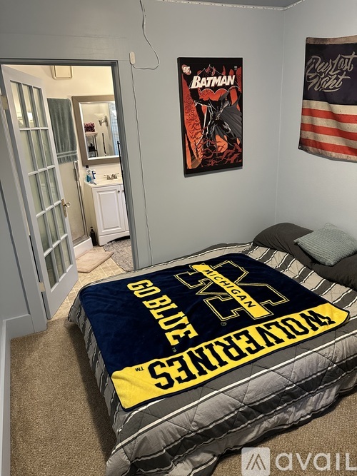 A bedroom with a bed covered in a blue and grey comforter with the letters "BUC" on it.
