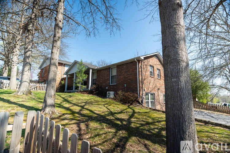 A house with a brown brick exterior is surrounded by a wooden fence and trees.