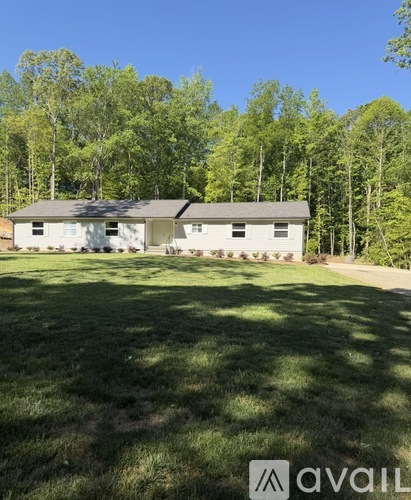 A house with a white exterior is surrounded by a grassy lawn and trees.