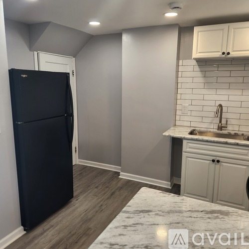 A black refrigerator is in a kitchen with white cabinets and a marble countertop.