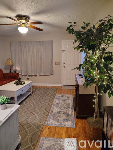 A living room with a ceiling fan and a tree with lights.