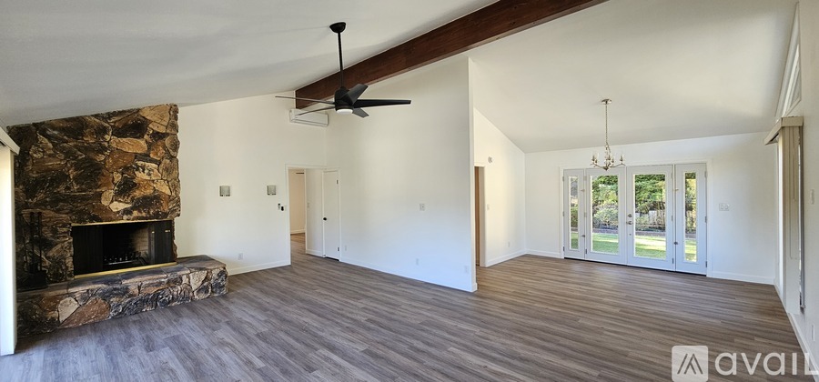A spacious living room with a stone fireplace and hardwood floors.