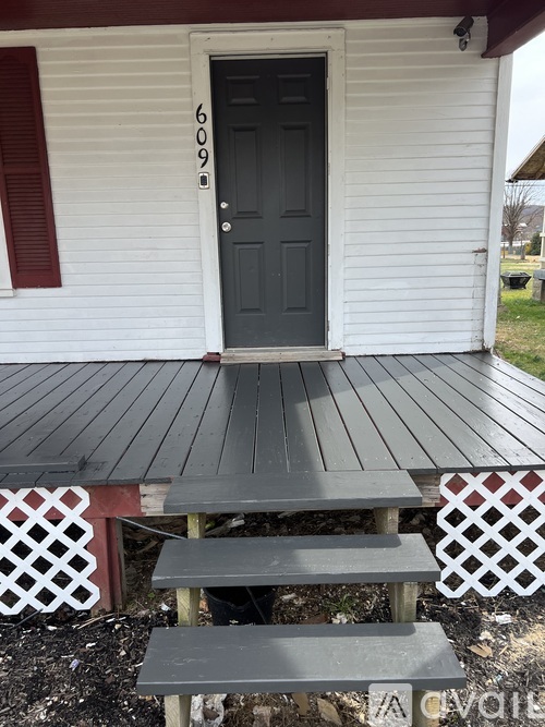 A white house with a black door and a grey deck.