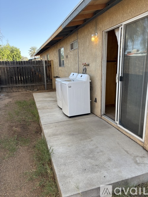 A white washing machine is placed on the concrete outside a house.