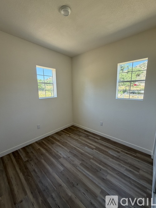 A room with wooden flooring and two windows.