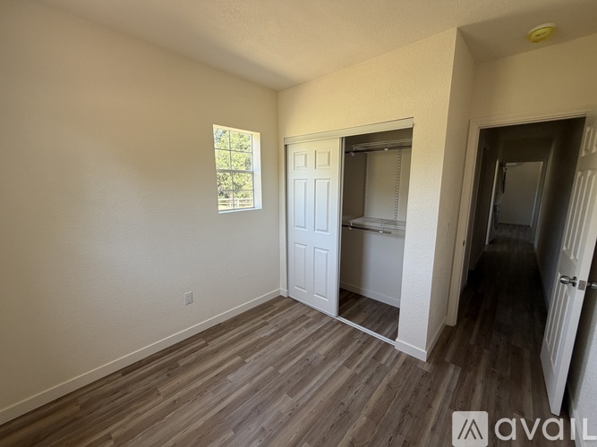 A room with wooden flooring and a window with a view of trees.