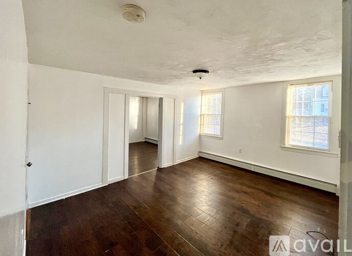 A room with wooden floors and white walls, with a window on the right side.