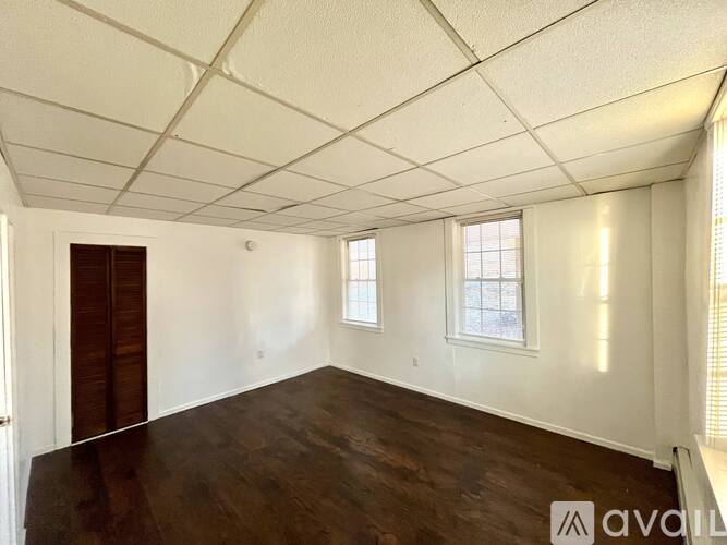 A room with wooden floors and white walls, with two windows and a door.