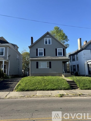 A house with a grey roof and a white door is in front of a tree.