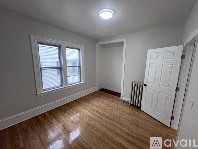 A room with wooden floors and white walls, with a window and a door.