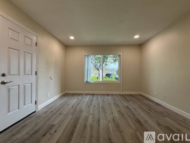 A room with a white door and a window with a view of trees.