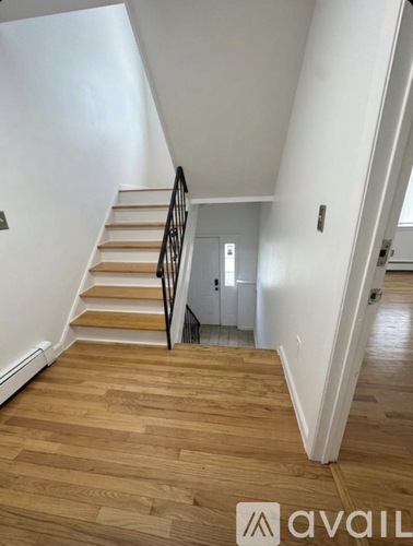 A wooden staircase with a black railing leads to a door at the end of the hallway.