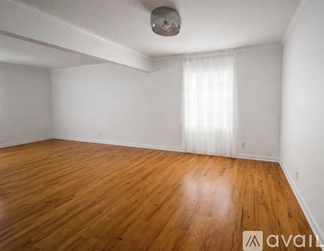 A room with wooden flooring and a window with white curtains.