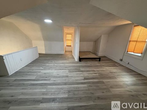 A spacious room with wooden flooring and a window with blinds.