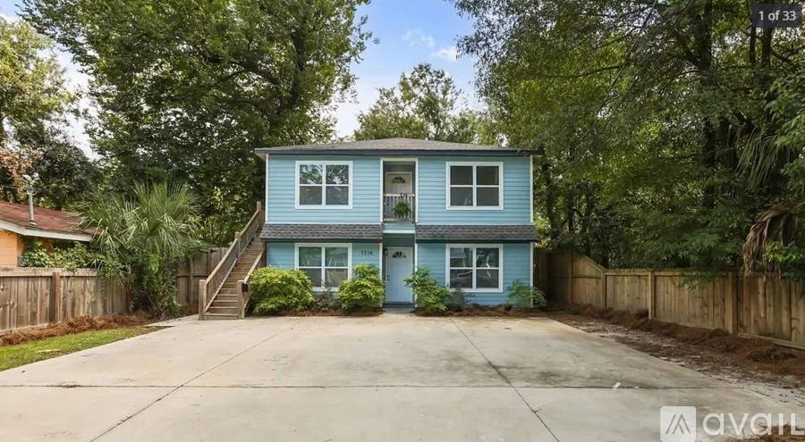 A blue house with a white fence and trees in the background.